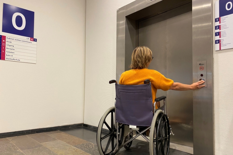 Afbeelding van een rolstoelgebruiker bij de lift in het Paleis van Justitie in Den Haag